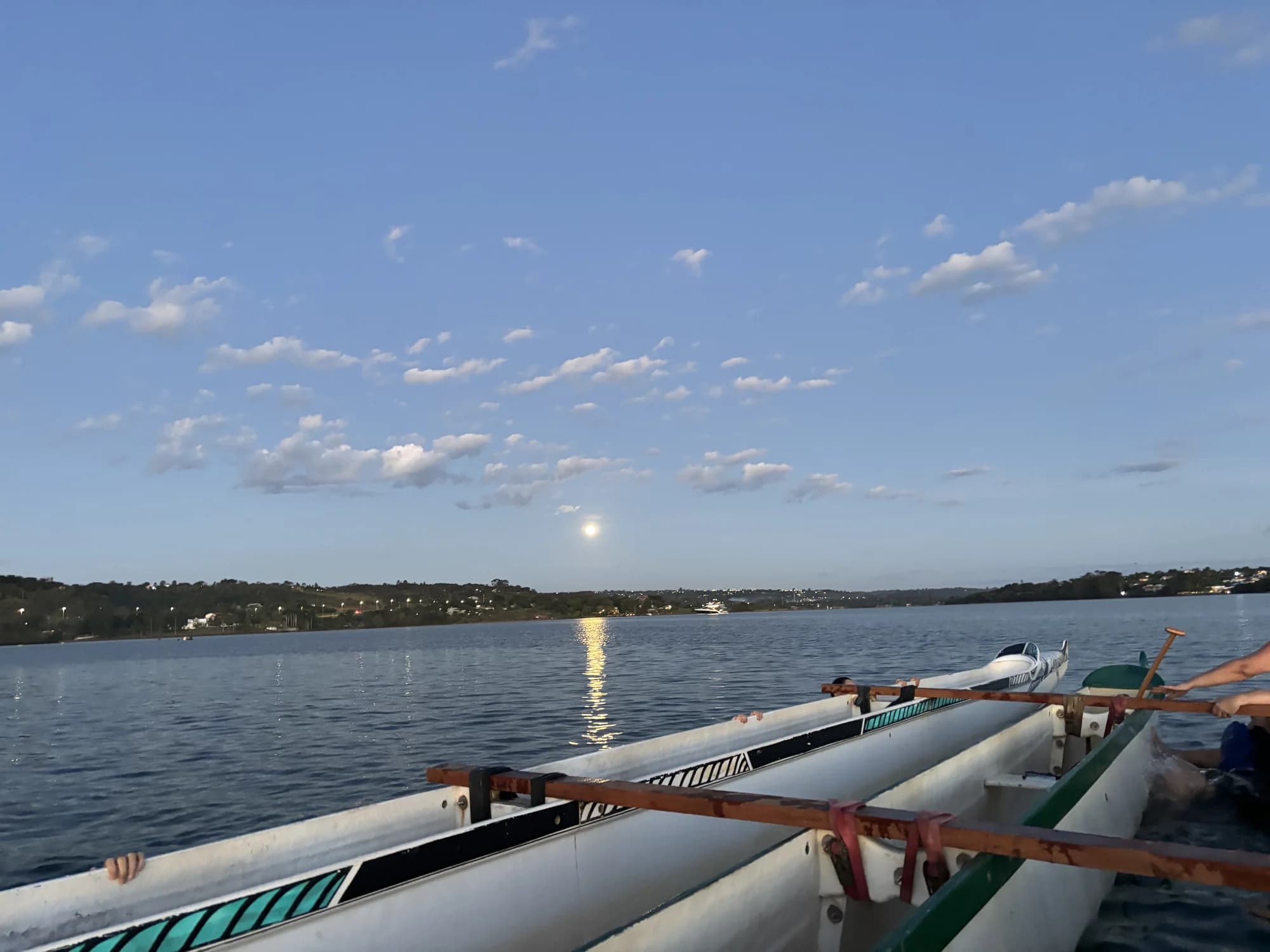 Lua cheia sobre canoas havaianas alinhadas na margem do Lago Paranoá