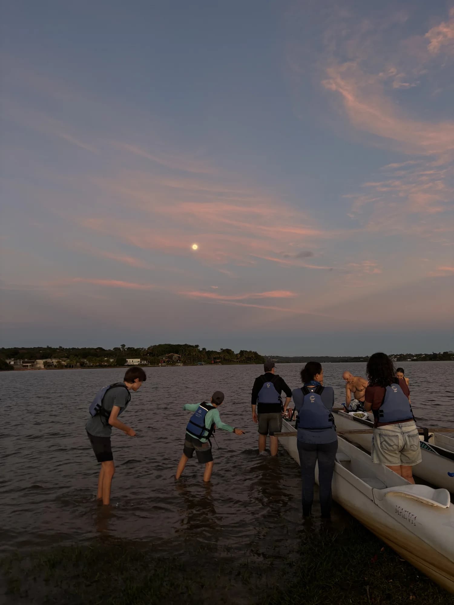 Participantes preparando canoas na margem do Lago Paranoá vistos de costas
