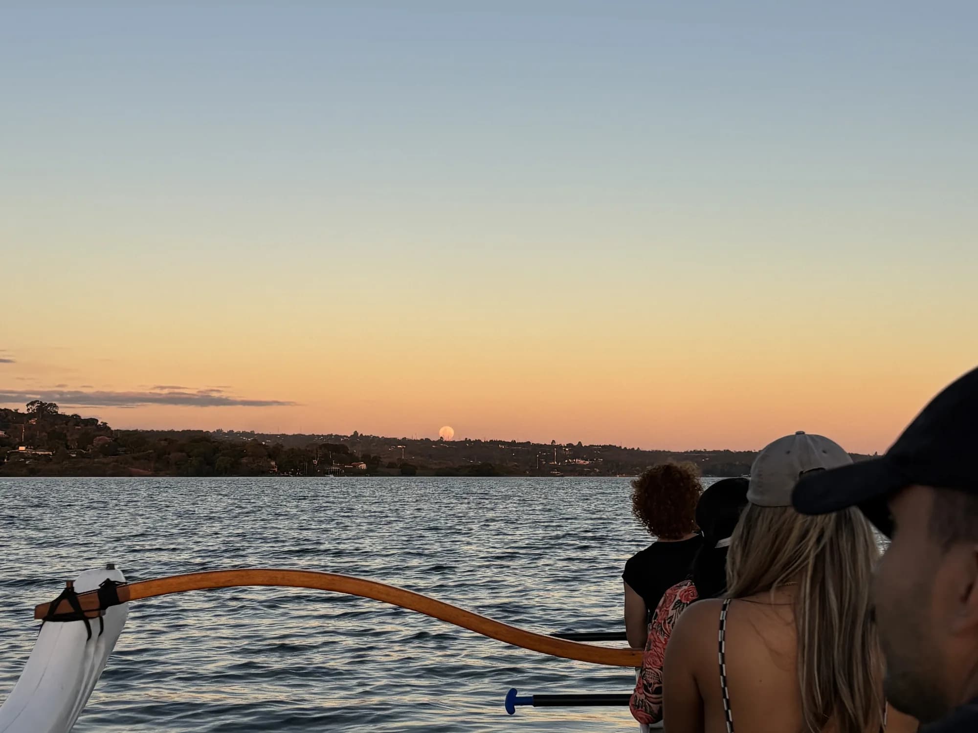 Remadores vistos de costas diante da lua cheia no horizonte