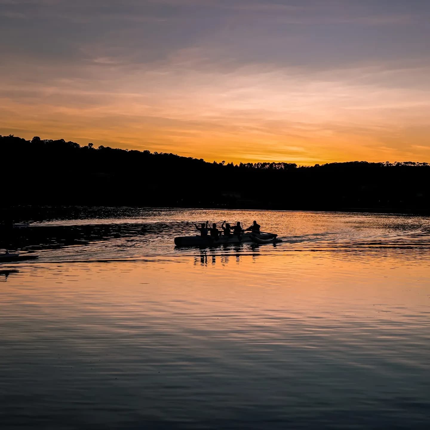 Canoa havaiana navegando sob o céu alaranjado do amanhecer