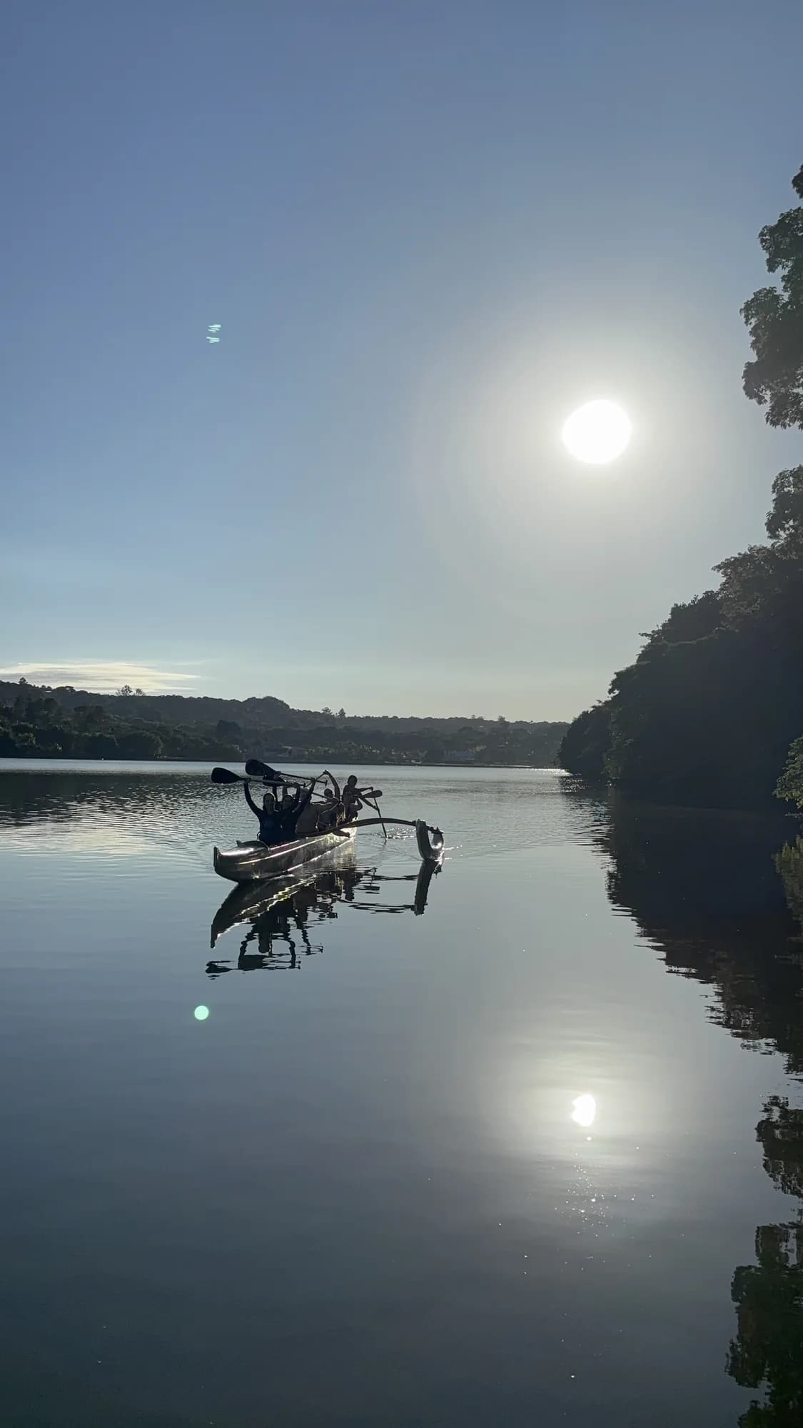 Canoa havaiana refletida nas águas calmas do Lago Paranoá pela manhã