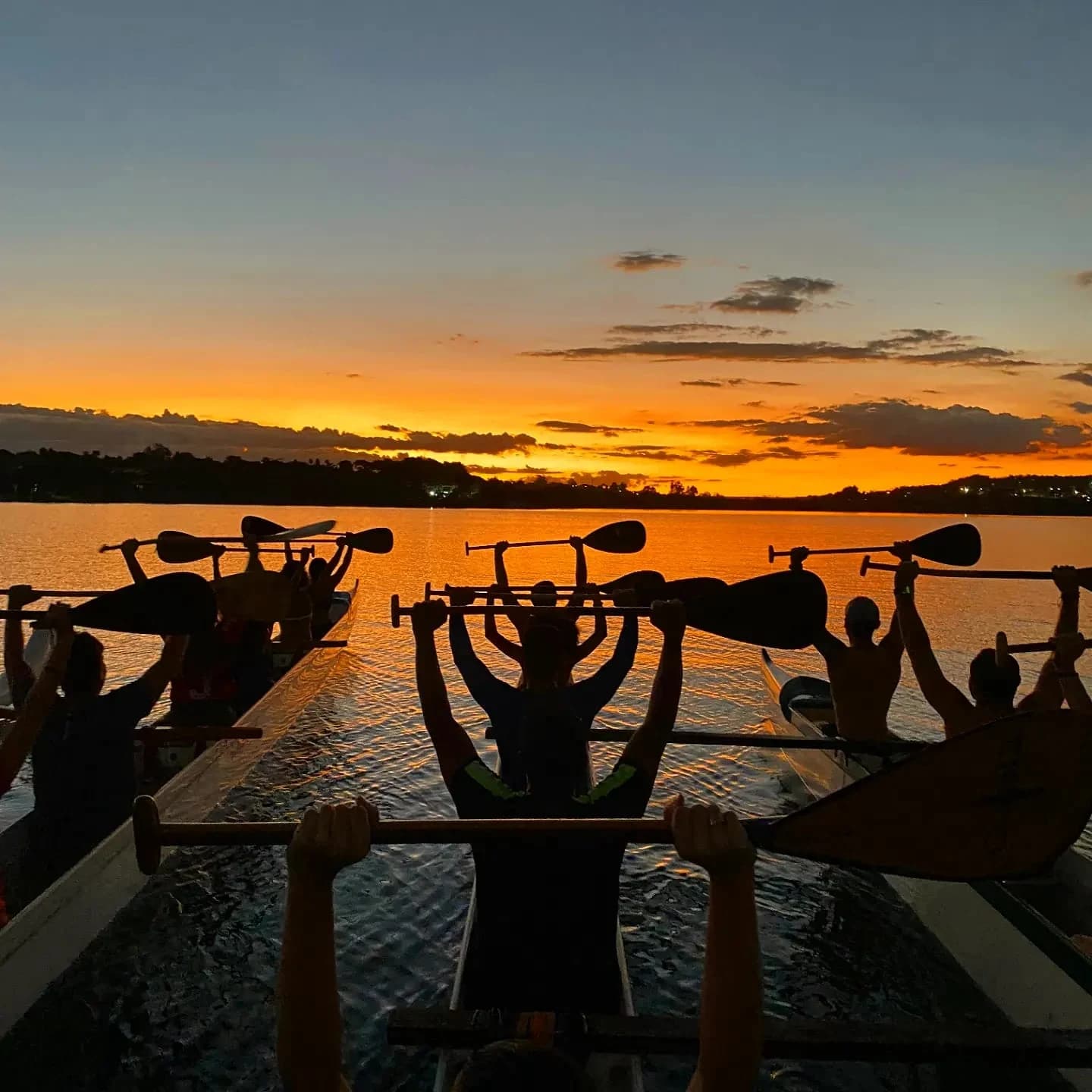 Participantes em canoas erguendo os remos diante do pôr do sol no Lago Paranoá