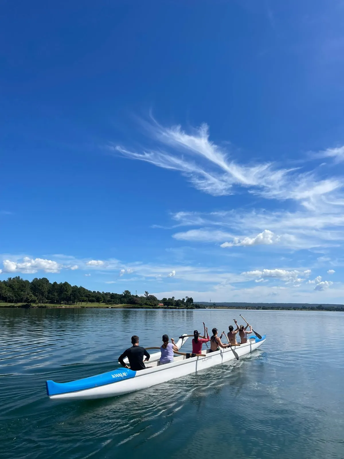 Grupo remando em canoa havaiana sob céu azul no Lago Paranoá