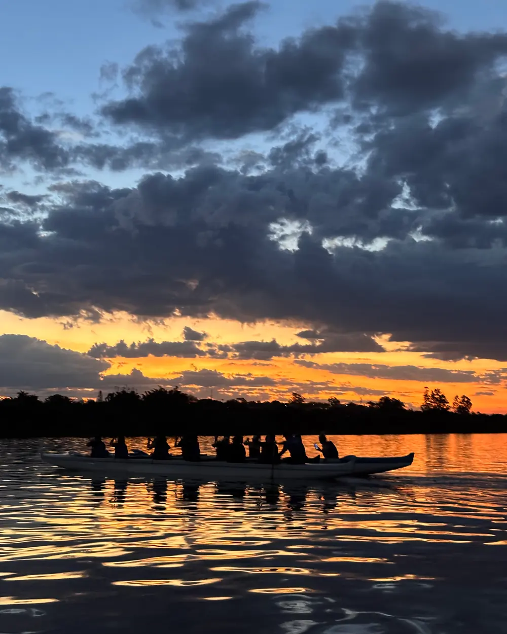 Canoa havaiana sob nuvens alaranjadas do pôr do sol no Lago Paranoá